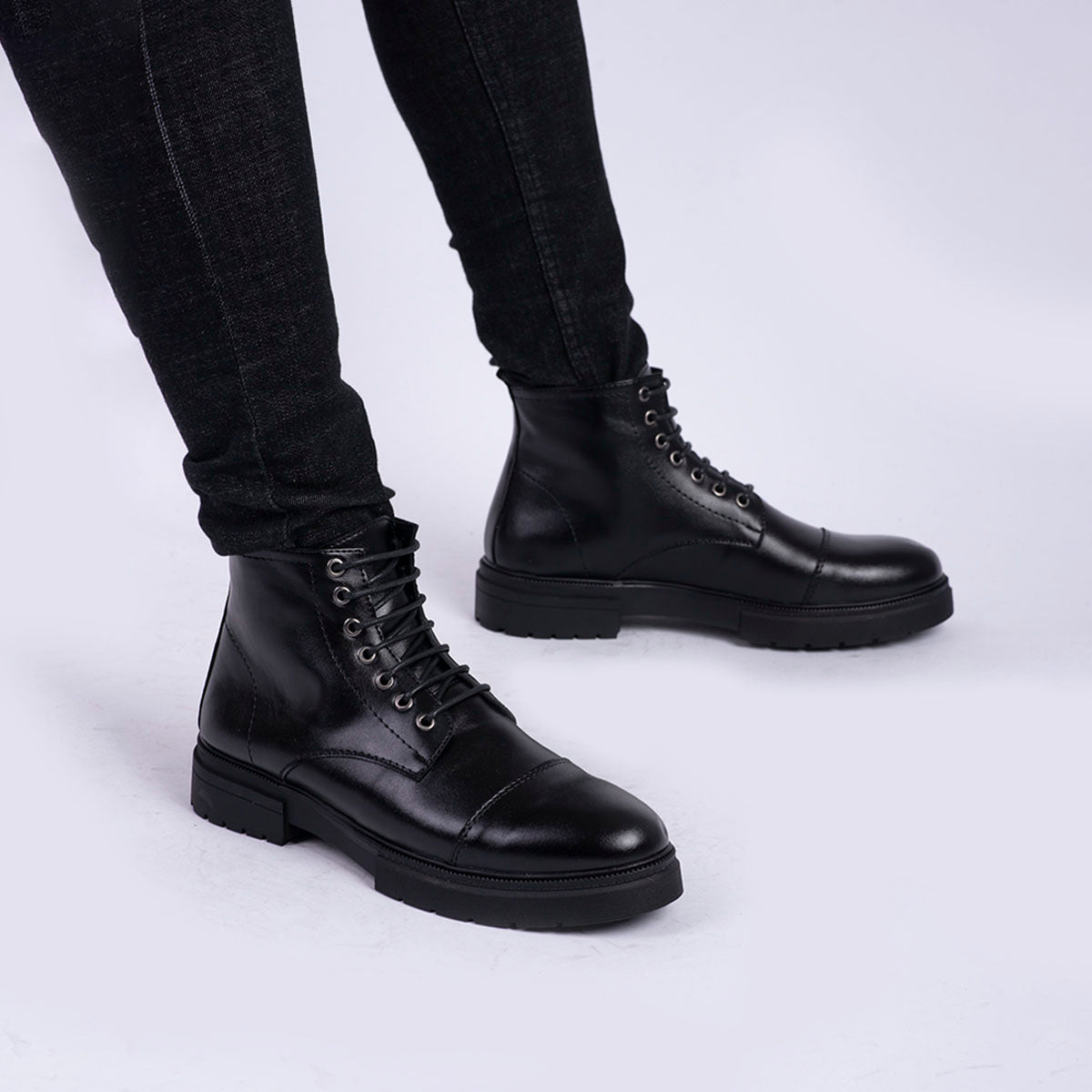 Black leather boots worn with black pants on a light gray background